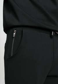 Joggers noirs en tissu texturé, avec une poche latérale zippée et une taille élastique pour le confort. Design minimaliste et coupe ajustée.