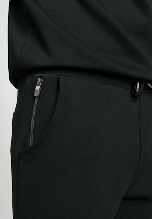 Joggers noirs en tissu texturé, avec une poche latérale zippée et une taille élastique pour le confort. Design minimaliste et coupe ajustée.