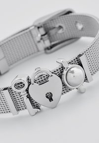 Bracciale in rete argentata con un lucchetto a forma di cuore, una chiave e un accento circolare. Finitura in metallo liscia con dettagli intricati sulle componenti metalliche.