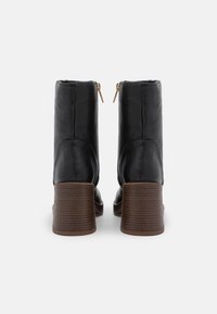 Bottines en cuir noir à talon bloc, avec une semelle texturée marron et des accents de fermeture éclair dorée à l'arrière.