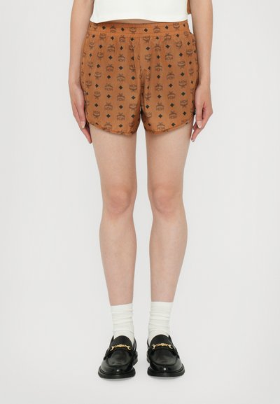 Shorts bruns avec un motif de couronne répétitif, une taille élastique et un tissu léger, assortis à des mocassins noirs et des chaussettes blanches.