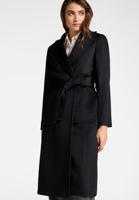 Cappotto avvolgente in lana nera con cintura annodata, ampi risvolti e due tasche frontali. Caratterizzato da un design strutturato e una texture liscia.