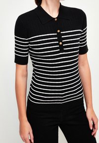 Polo en maille à rayures noires et blanches avec manches courtes, texture côtelée et trois boutons dorés au col.