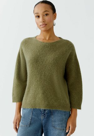 Olive green sweater made of soft, fuzzy material. Features a round neck, three-quarter sleeves, and a relaxed fit. Paired with blue jeans.