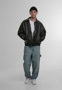 Black leather bomber jacket with oversized fit, featuring a ribbed collar and cuffs. Worn over a white t-shirt, paired with light blue baggy jeans.