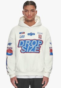 Felpa bianca con cappuccio caratterizzata da una grande grafica "DROP SIZE" blu e rossa, numerosi toppe, tasca frontale e polsini a costine.