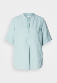 Blouse bleu clair à manches courtes avec col mandarin et ouverture fendue devant, en tissu texturé.