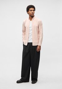 Ροζ πουκάμισο με κουμπιά, μακριά μανίκια, γιακάς, συνδυασμένο με άνετο μαύρο παντελόνι και μαύρα παπούτσια. Απλό, υφασμάτινο ύφασμα με υφή.