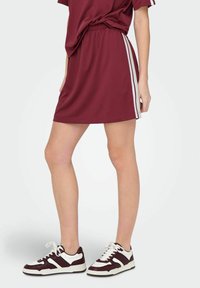 Bordeauxkleurige sportjurk met korte mouwen, elastische tailleband en witte zijstrepen. Gecombineerd met donkerbordeauxkleurige en witte sneakers.