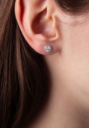 Okrągłe kolczyki wkręty z przezroczystym centralnym kamieniem otoczonym srebrnym halo. Kolczyki osadzone są w wypolerowanym metalu.