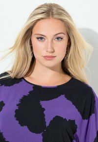 Väljä musta toppi, jossa on violetti abstrakti kuvio. Pyöreä pääntie ja pehmeä kangas luovat rentoon ilmeen.