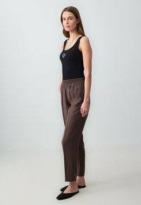 Zwarte geribbelde tanktop gecombineerd met een paar bruine losse broek. De outfit heeft een relaxte tailleband en platte zwarte instappers.