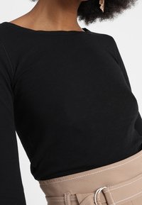 Černý dlouhý rukáv top s širokým výstřihem, mírně elastická tkanina, spárovaný se světle béžovou sukní se zřetelným švem a páskem.