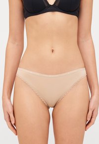 Culotte de bikini beige avec dentelle, finition douce et ceinture en logo. Le tissu est lisse, mettant en valeur le délicat détail de l'ourlet.
