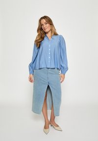 Hele sinine nööpidega pluus koos puhviga varrukatega, kombineeritud hele sinine teksaseelik, millel on esi lõhik. Beezid terava ninaga kõrged kontsad.