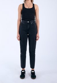 Svart ribbad linne, högmidjade svarta jeans med en figursydd siluett, och mörka sneakers med vita accenter. Enkelt, avslappnat outfit.