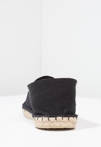 Black canvas espadrille with a woven jute sole, featuring a rounded back and soft textile upper, designed for comfort and casual wear.