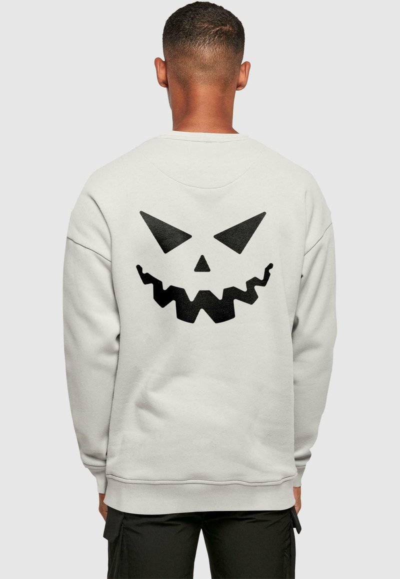 Ljust grå sweatshirt med en stor svart pumpaansikte-grafik på baksidan. Tillverkad av mjukt tyg med långa ärmar och rundad hals.