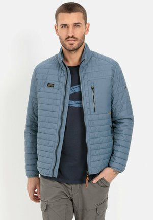 Light blue quilted jacket with zippered pockets and a high collar. Features a tag on the chest and a subtle pattern on the fabric.