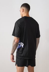 Schwarzes Sport-T-Shirt mit lockerer Passform; hat kurze Ärmel und ein blaues Grafikdesign auf der linken Seite; glatte Textur.