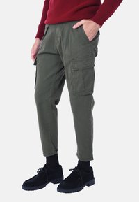 Pantaloni cargo verde oliva con molte tasche laterali, vestibilità tapered e vita elastica. Abbinati a scarpe nere stringate.