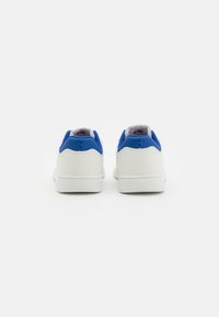 Weiße Ledersneaker mit einem blauen Akzent an der Ferse, die eine glatte Textur, eine abgerundete Form und sichtbare Gummisohlen aufweisen.