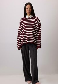 Maglione oversize a righe bordeaux e bianche con scollo a V, abbinato a pantaloni larghi scuri e sneakers rosa chiaro. Tessuto a maglia testurizzato.