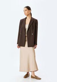 Brun dobbeltradet blazer over en beige tætsiddende kjole, stylet med tørrede brune loafers. Minimalistisk design, glat stof, skræddersyet pasform.