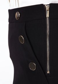 Svart kjol med en figursydd design, som har en silvrig dragkedja och rund metallknappar, tillverkad av ett slätt tyg med en lätt lyster.