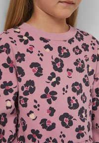 Rosa Sweatshirt mit floralen Mustern in Schwarz, Kastanienbraun und Blassgelb. Gerippter Ausschnitt und weicher, strukturierter Stoff.