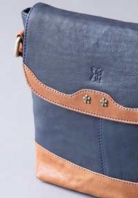 Leather messenger bag featuring a navy top with a tan bottom section, accented by decorative stitching and metallic studs.