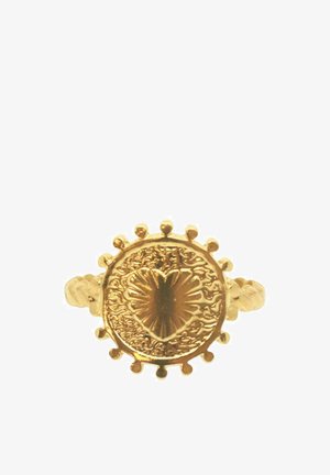 Anello d'oro con una faccia circolare testurizzata che presenta un design a forma di cuore, circondato da piccole punte; la fascia attorcigliata aggiunge dimensione.