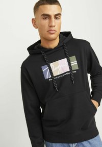 Black hooded sweatshirt with contrasting drawstrings, front pocket, and colorful graphic design featuring text in various pastel shades.