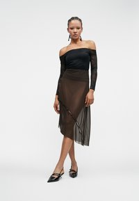 Melnas mežģīnes off-shoulder topiņš, apvienots ar caurspīdīgu brūnu asimetrisku svārku, kam ir pogu akcenti un sudraba melnas lakotas zābaciņas.