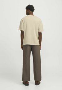 Beige oversized t-shirt med korte ærmer, afslappet pasform, parret med brune vide bukser, båret med mørke sandaler.