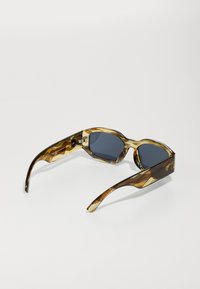 Gafas de sol de carey con montura angular, lentes oscuros y un acabado brillante. Textura y patrón notables en el diseño de la montura.