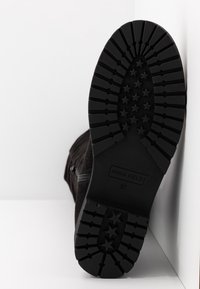 Semelle de bottine noire avec une bande de roulement profonde présentant des motifs en forme d'étoile et la mention de taille "ANNA FIELD 37", présentée sur un fond blanc.