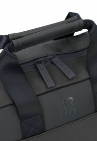 Bolsa de viaje negra con un exterior liso, fabricada con tejido resistente, cierres de doble cremallera y una marca en relieve. Las asas están acolchadas para mayor comodidad.