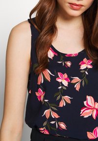 Débardeur bleu marine orné d'un motif floral avec des fleurs roses et crème ; encolure arrondie et tissu doux et léger.