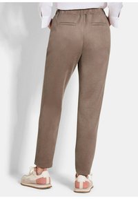 Bruine, taps toelopende broek met een elastische tailleband, twee achterzakken en een gladde textuur, gecombineerd met lichtgekleurde sportschoenen.
