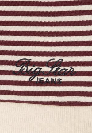 Burgundi ja kreemika triibuline kangas, millel on tumepunasega tikitud "Big Star" üle "JEANS." Pehme tekstuur ja soonikserv.