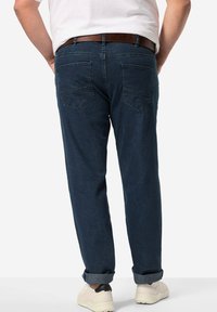 Jeans de mezclilla azul oscuro con un corte relajado, que cuentan con dos bolsillos traseros, un cinturón de cuero y puños enrollados. Textura suave y costuras resistentes.