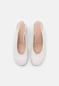 Pár bílých dámských bot na podpatku s kulatými čtvercovými špičkami a béžovými paměťovými gelovými vložkami s vytlačeným nápisem "wonders."