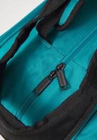 Türkiser Innenraum der Tasche mit schwarzen Reißverschlüssen; verfügt über doppelte Schieber und strukturierten Stoff. Enthält kontrastierende schwarze Träger und Nähte.