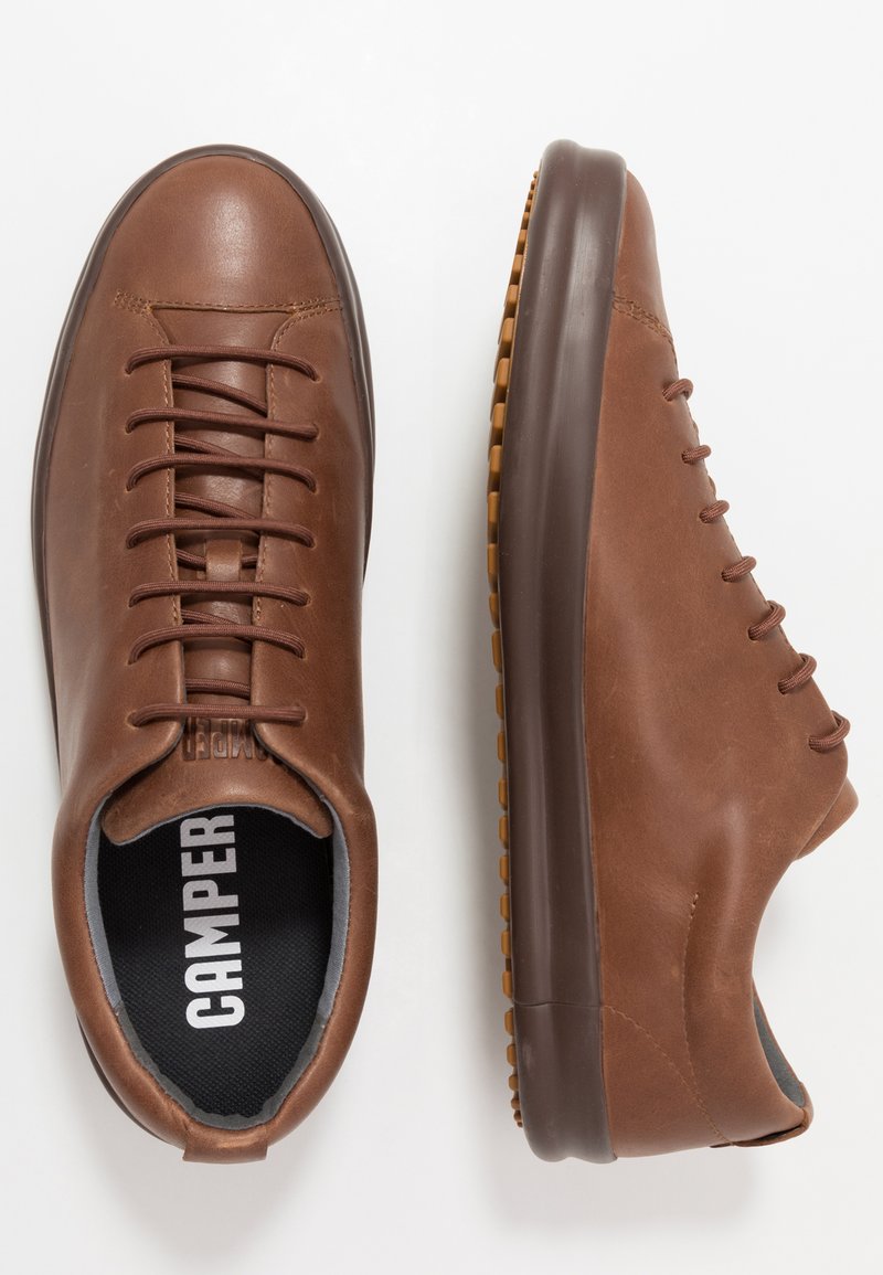 Zapatillas de cuero marrón con cordones, acabado suave, suela de goma y forro interior gris con el nombre de la marca "Camper."