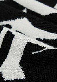 Tessuto lavorato a maglia in bianco e nero con un motivo astratto audace. La trama è morbida con punti visibili e un aspetto tessuto distinto.