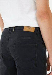 Zwarte denim broek met een getextureerde afwerking, voorzien van een tan leren label, een vijf-pocket ontwerp en zichtbare stikseldetails.