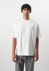 Hvid bomulds t-shirt med rund halsudskæring og korte ærmer, med teksten "don't waste culture" i sort på venstre bryst.