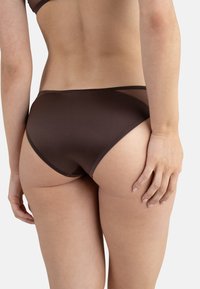 Culotte de bikini marron en matériau lisse. Présente des panneaux transparents et des détails de couture subtils. La vue arrière montre un design à cuisse haute.