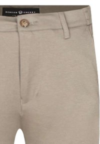 Pantalon en coton beige à jambe droite, avec une fermeture à un bouton et des passants de ceinture. Texture lisse avec un minimum de détails.